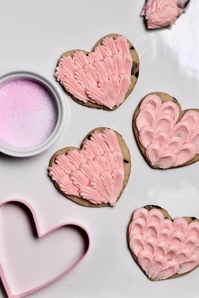 pink frosted cookies, in the shapes of hearts, sitting on a white platter