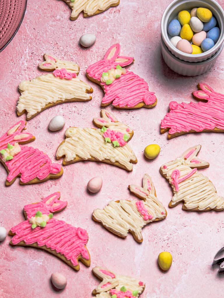 Overhead of pink and white bunny cookies decorated with buttercream, sitting on a pink background.