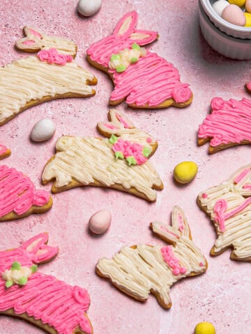 Overhead of pink and white bunny cookies decorated with buttercream, sitting on a pink background.