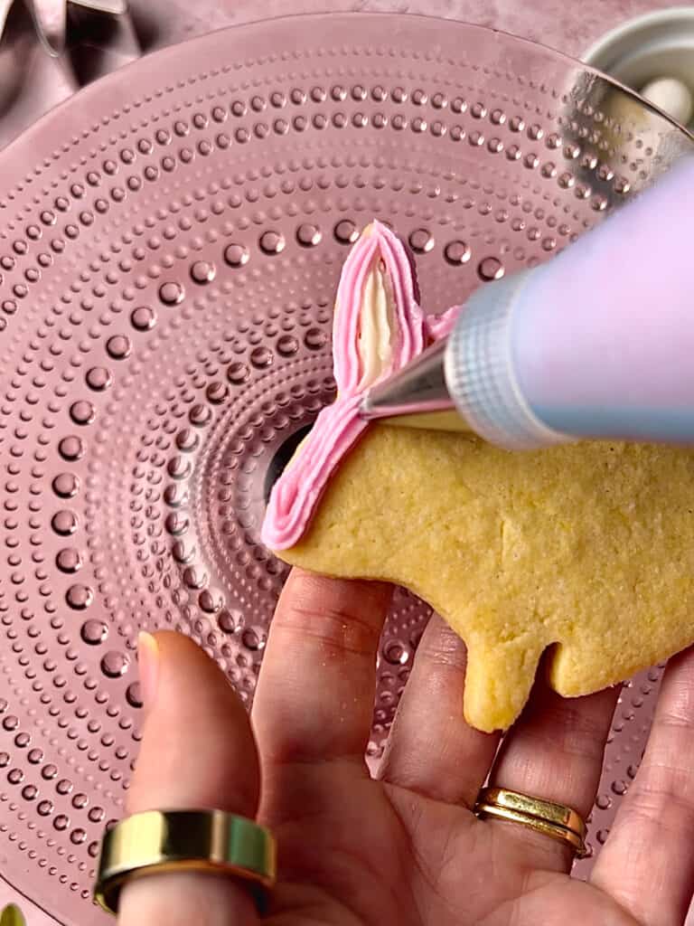 action shot of piping bag decorating a pink bunny cookie on a pink background