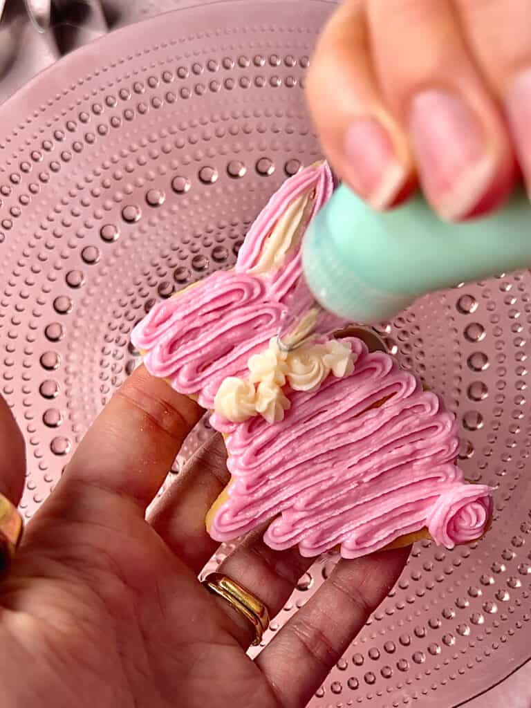 action shot of piping bag decorating a pink bunny cookie on a pink background