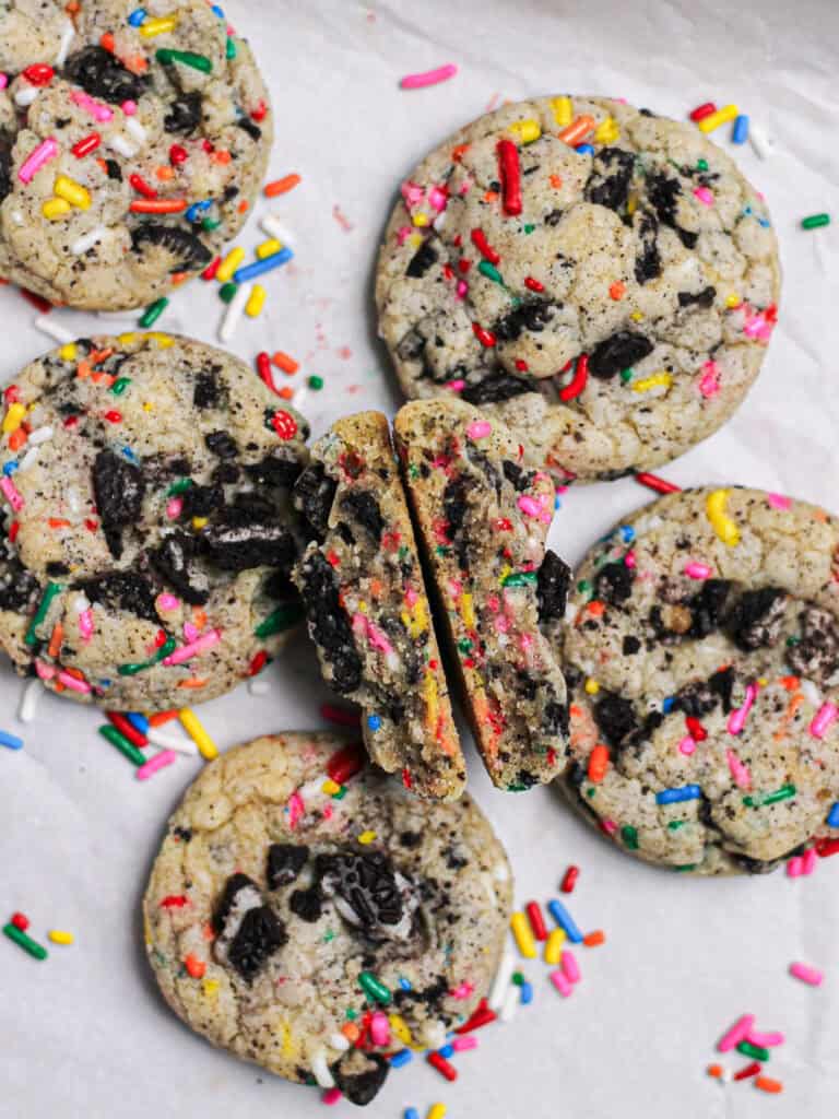 Oreo Funfetti cookie broken in half so that the inside is facing up toward the camera and is surrounded by more cookies and sprinkles.