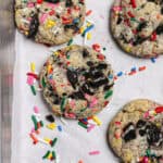 Cookies with rainbow sprinkles and Oreo pieces, sitting on a white piece of parchment.