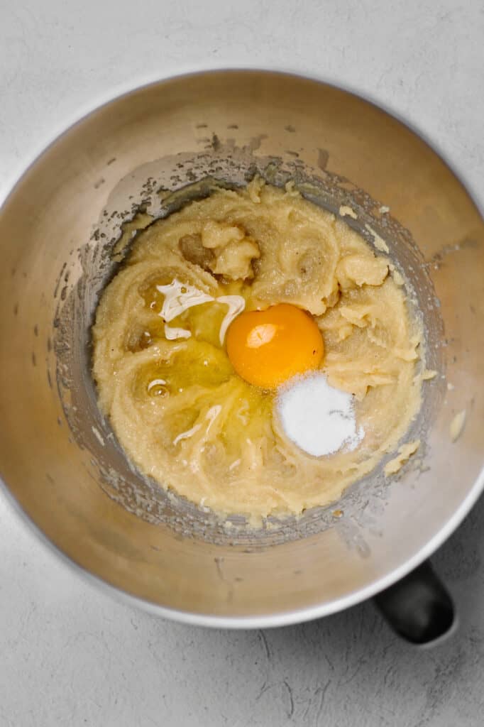 mixing bowl full of light colored cookie dough and an egg