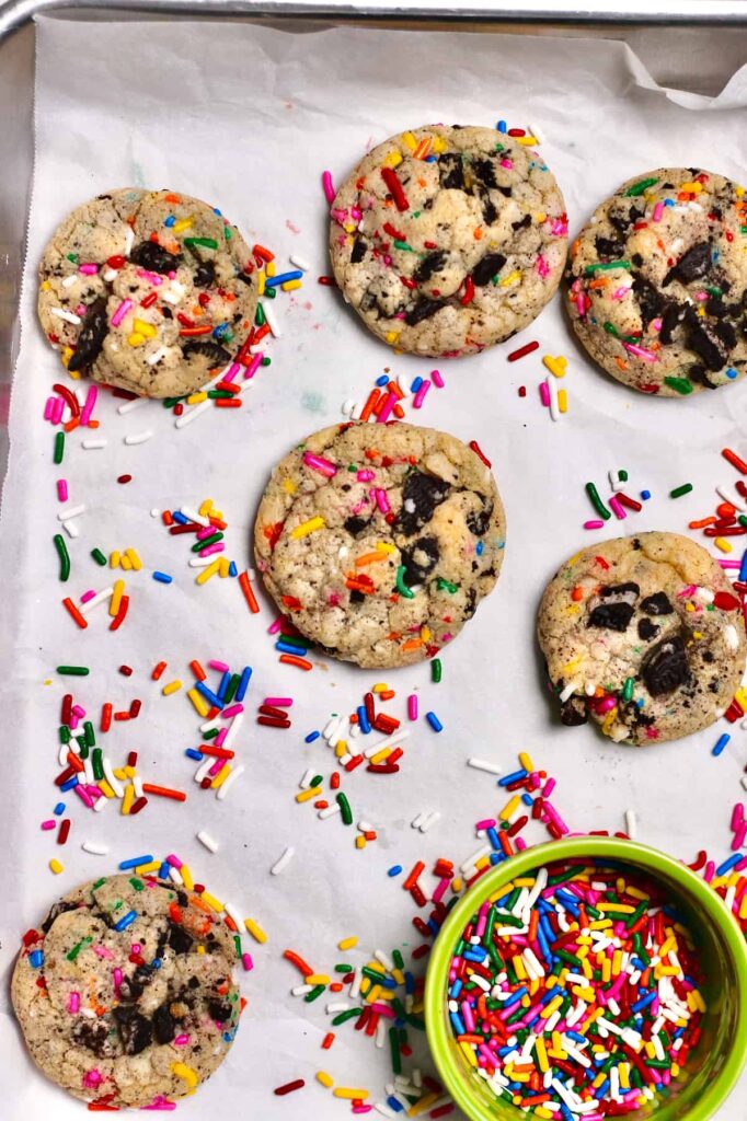 cookies with rainbow sprinkles and Oreo pieces, sitting on a white piece of parchment