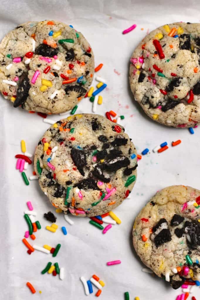cookies with rainbow sprinkles and Oreo pieces, sitting on a white piece of parchment