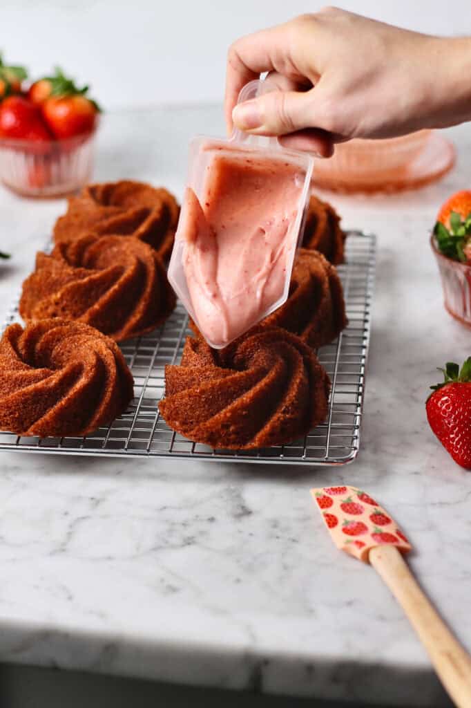 pouring strawberry cream cheese icing onto mini bundt cakes