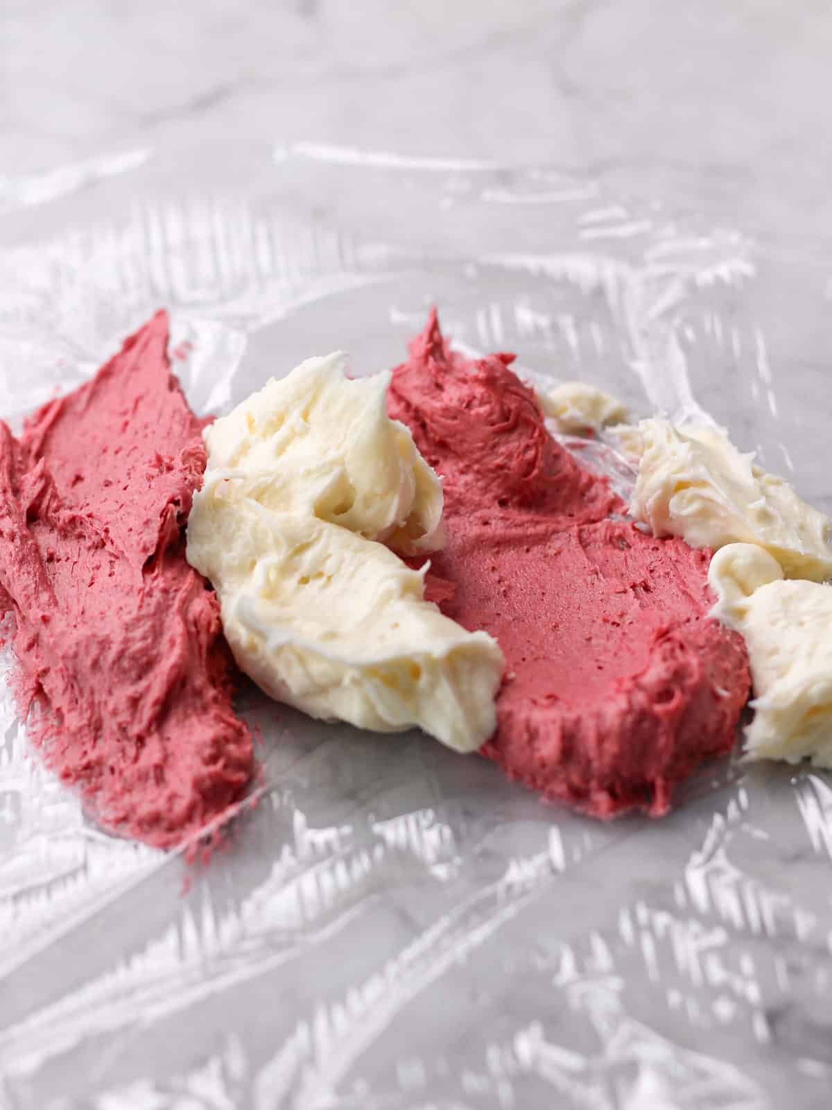 plastic wrap laid flat on a counter with marbled raspberry and cream cheese frosting on top of it.