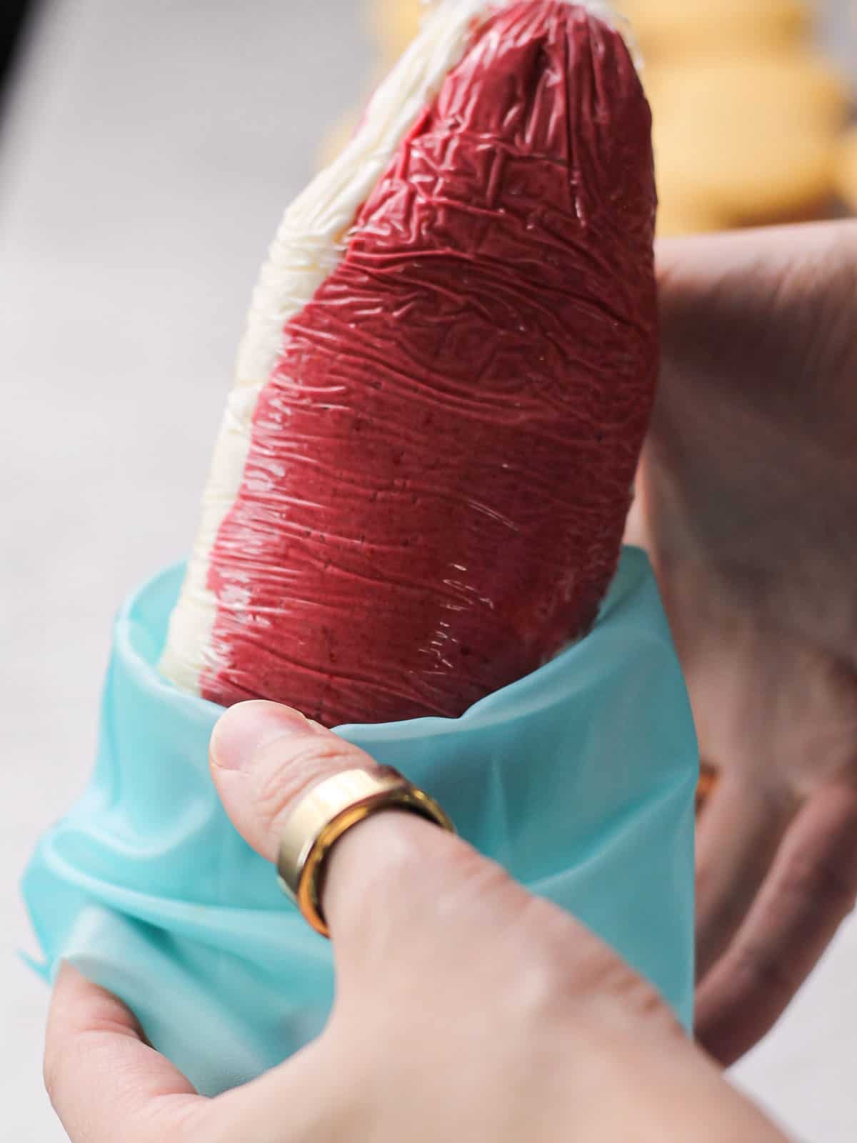 fitting a sleeve of plastic wrap into a piping bag of marbled raspberry and cream cheese frosting.