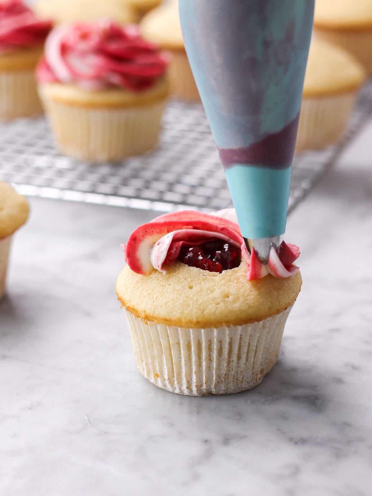 action shot of piping marbled raspberry frosting onto a cupcake