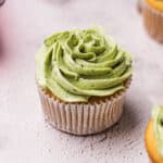 vanilla cupcake in a white cupcake liner with green frosting swirled on top of it.