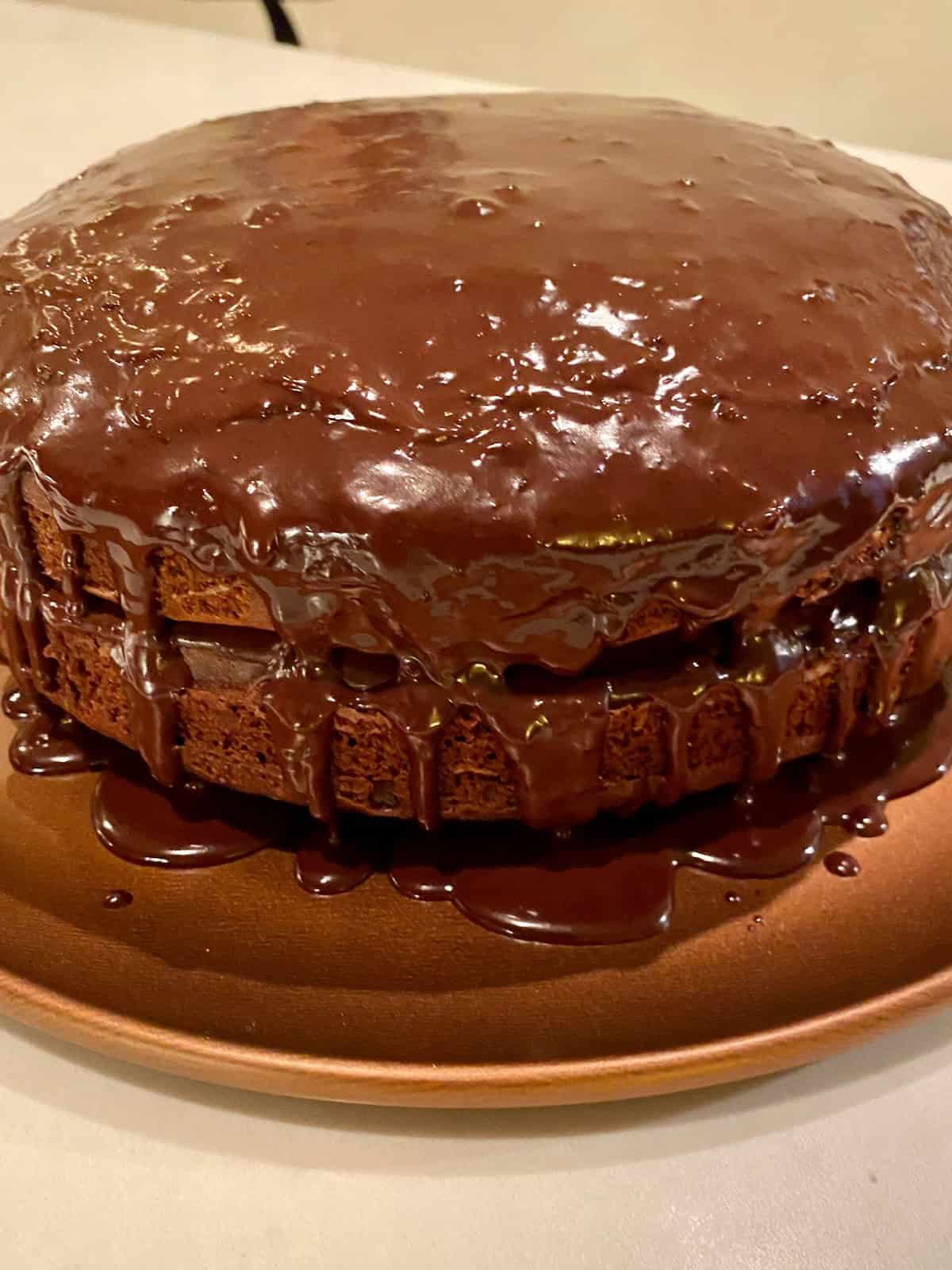 Two layer chocolate cake with glaze, sitting on a brown platter.