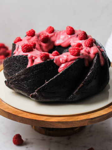 chocolate Bundt cake, coated with a pink raspberry cream cheese glaze and fresh raspberries on top.