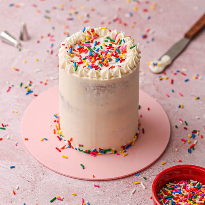 A small white cake filled and covered with rainbow sprinkles.