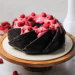 Chocolate Bundt cake, coated with a pink raspberry cream cheese glaze and fresh raspberries on top.