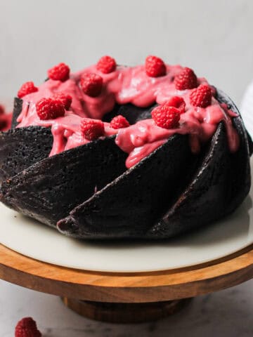 Chocolate Bundt cake, coated with a pink raspberry cream cheese glaze and fresh raspberries on top.