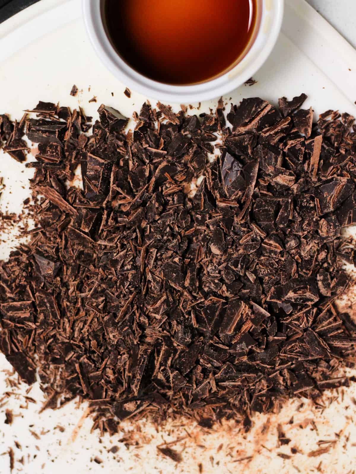 Pieces of chopped chocolate on a cutting board, next to vanilla extract