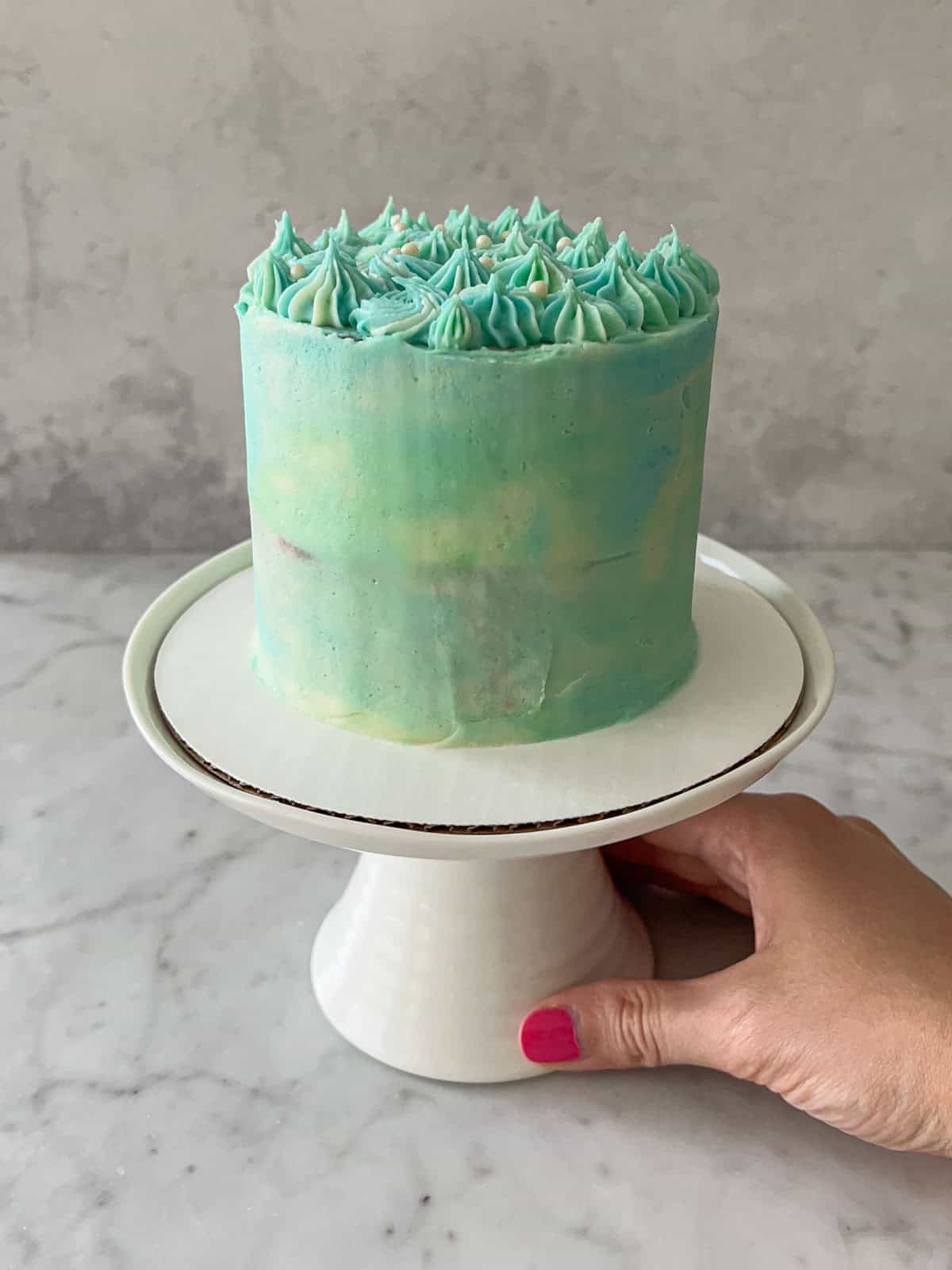 Blue smash cake on a white cake stand, held be a hand for a baby's birthday.