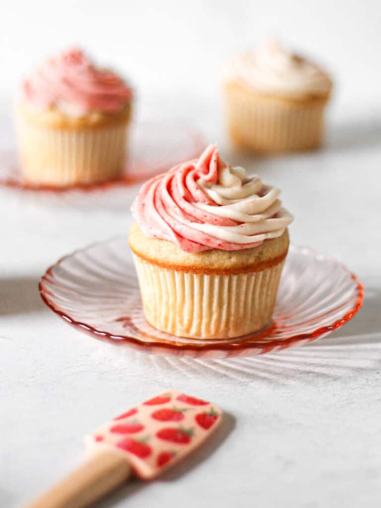Strawberry filled cupcake sitting on a small pink plate, with a mini spatula next to it.