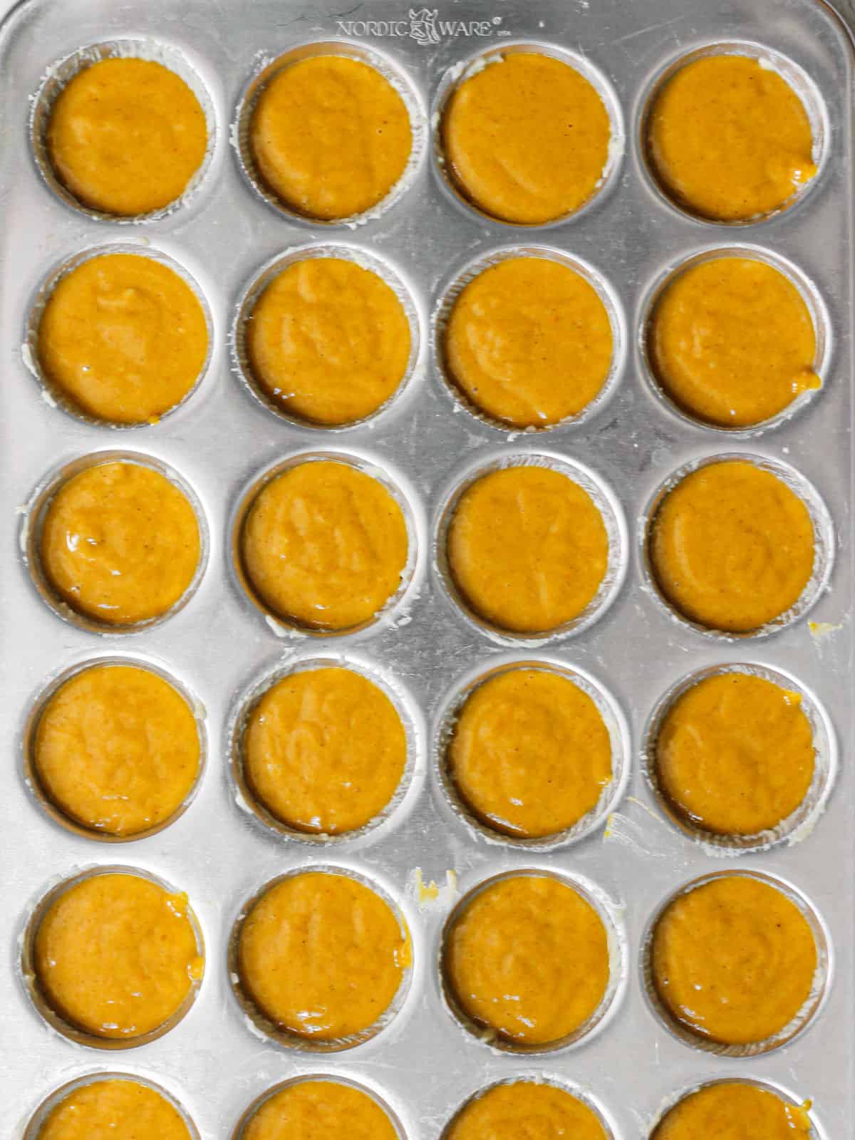 Overhead shot of mini muffin tin, filled with pumpkin muffin batter.