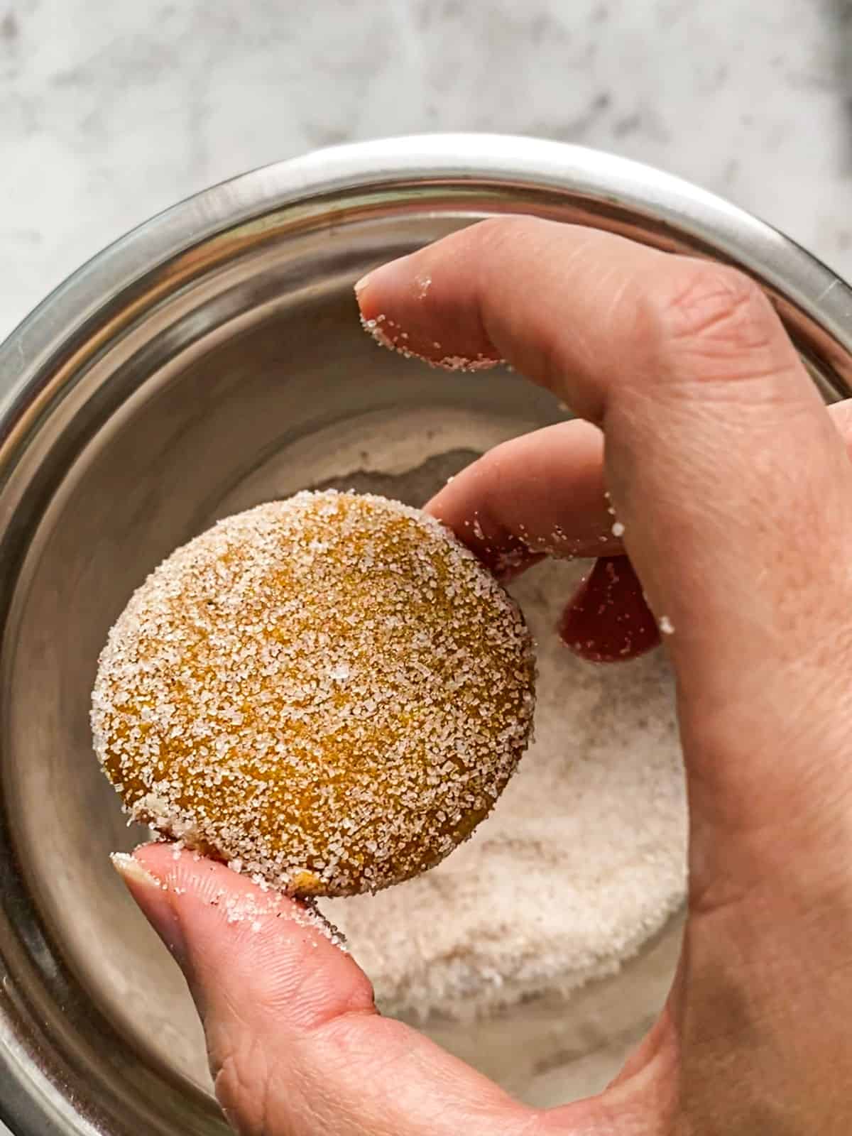 Rolling mini pumpkin muffin in cinnamon sugar mixture.