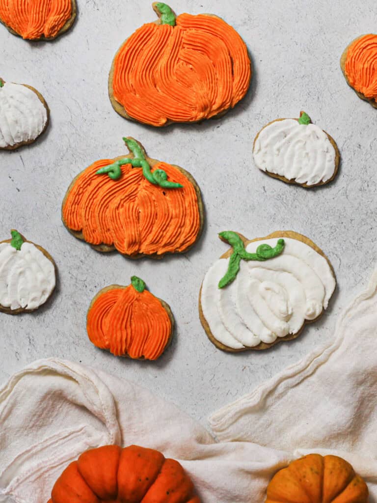 Overhead image of decorated pumpkin sugar cookies, piped in orange and white frostings.