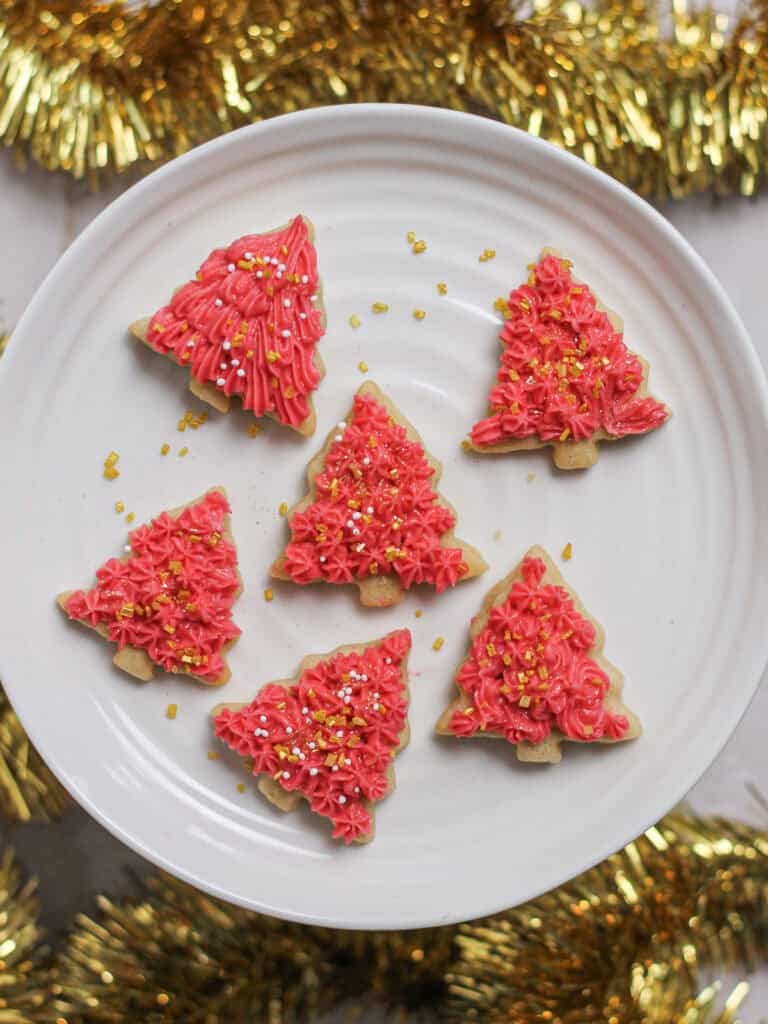 Mini Christmas tree sugar cookies, decorated with sprinkles and pink buttercream.