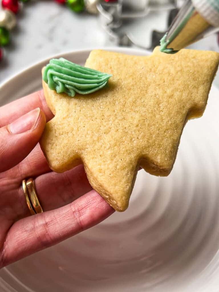 Process shot of piping frosting onto Christmas tree sugar cookies.