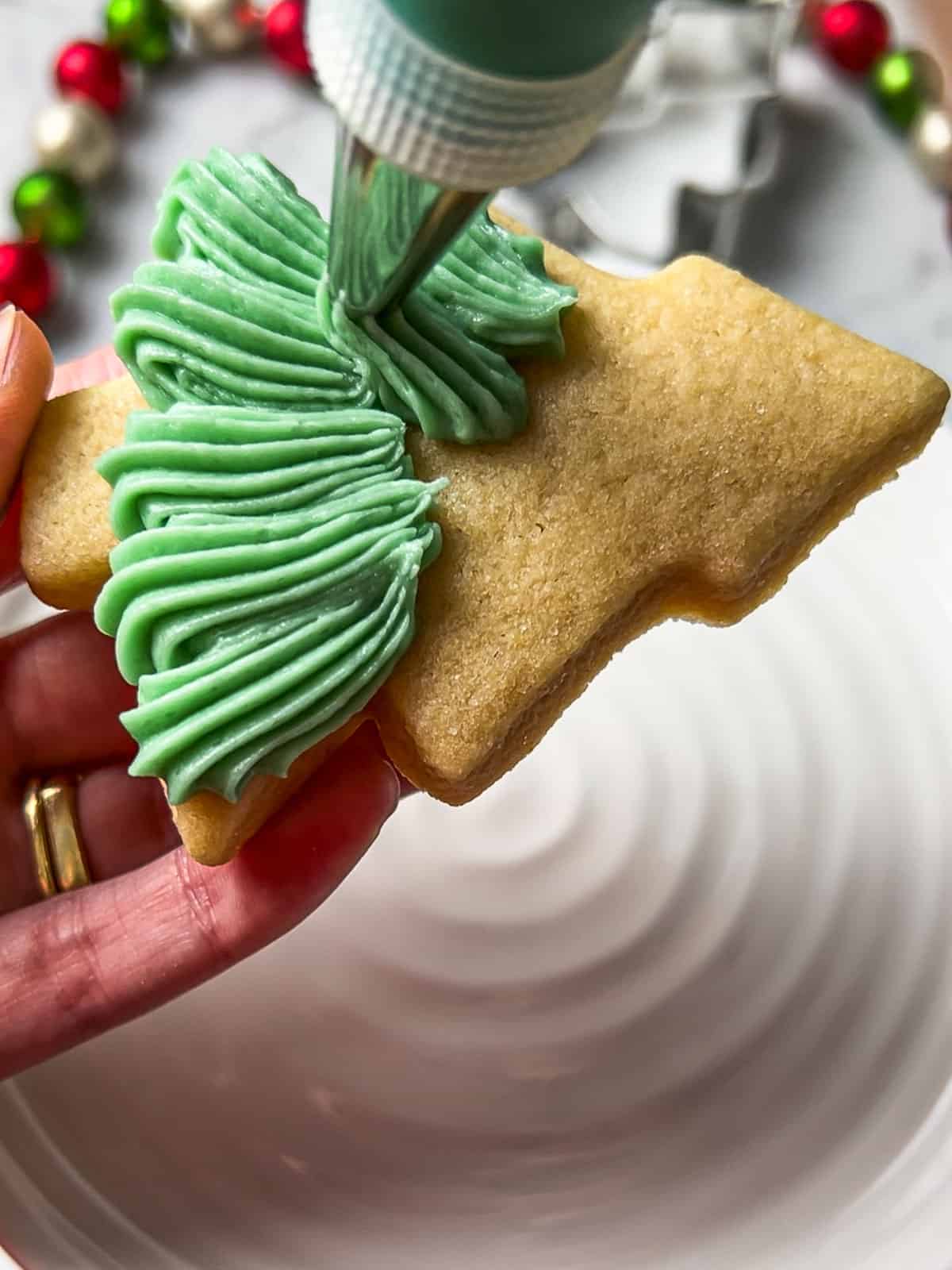 Process shot of piping frosting onto a Christmas tree sugar cookie.