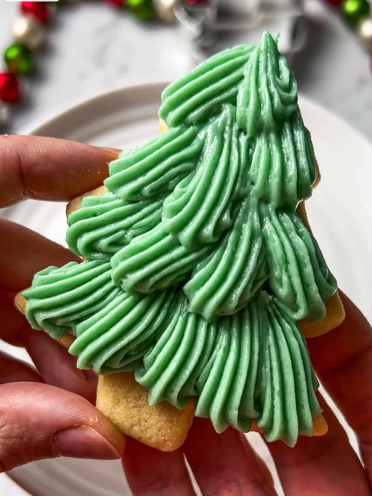 Pair of hands holding a decorated Christmas tree sugar cookie.