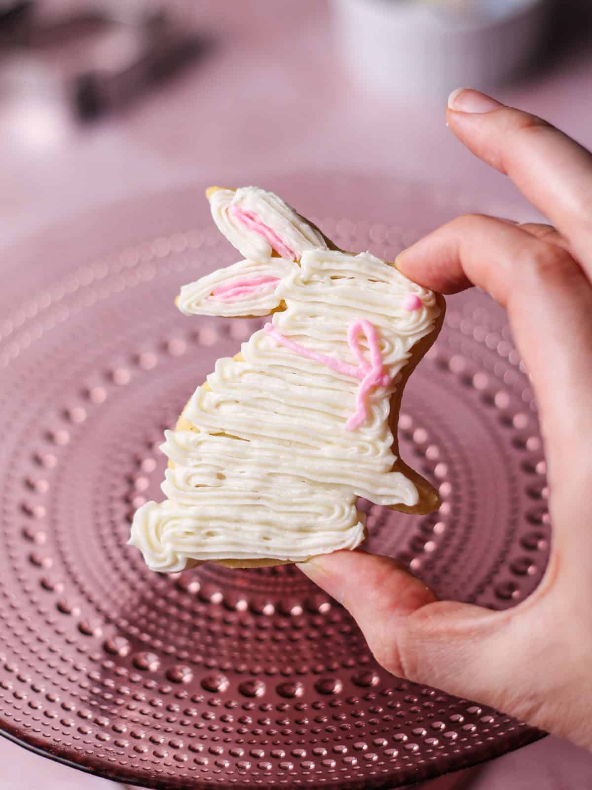 Frosted white bunny sugar cookie with a pink bow of frosting around its neck.