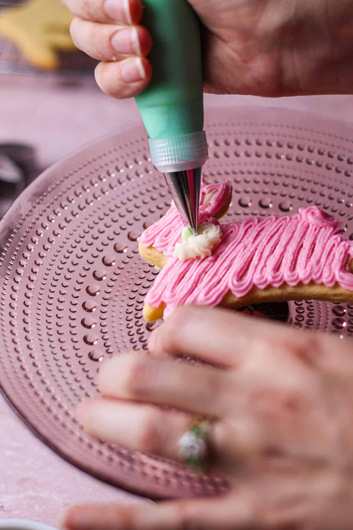 Action shot of piping bag decorating a pink Easter bunny sugar cookie on a pink background.
