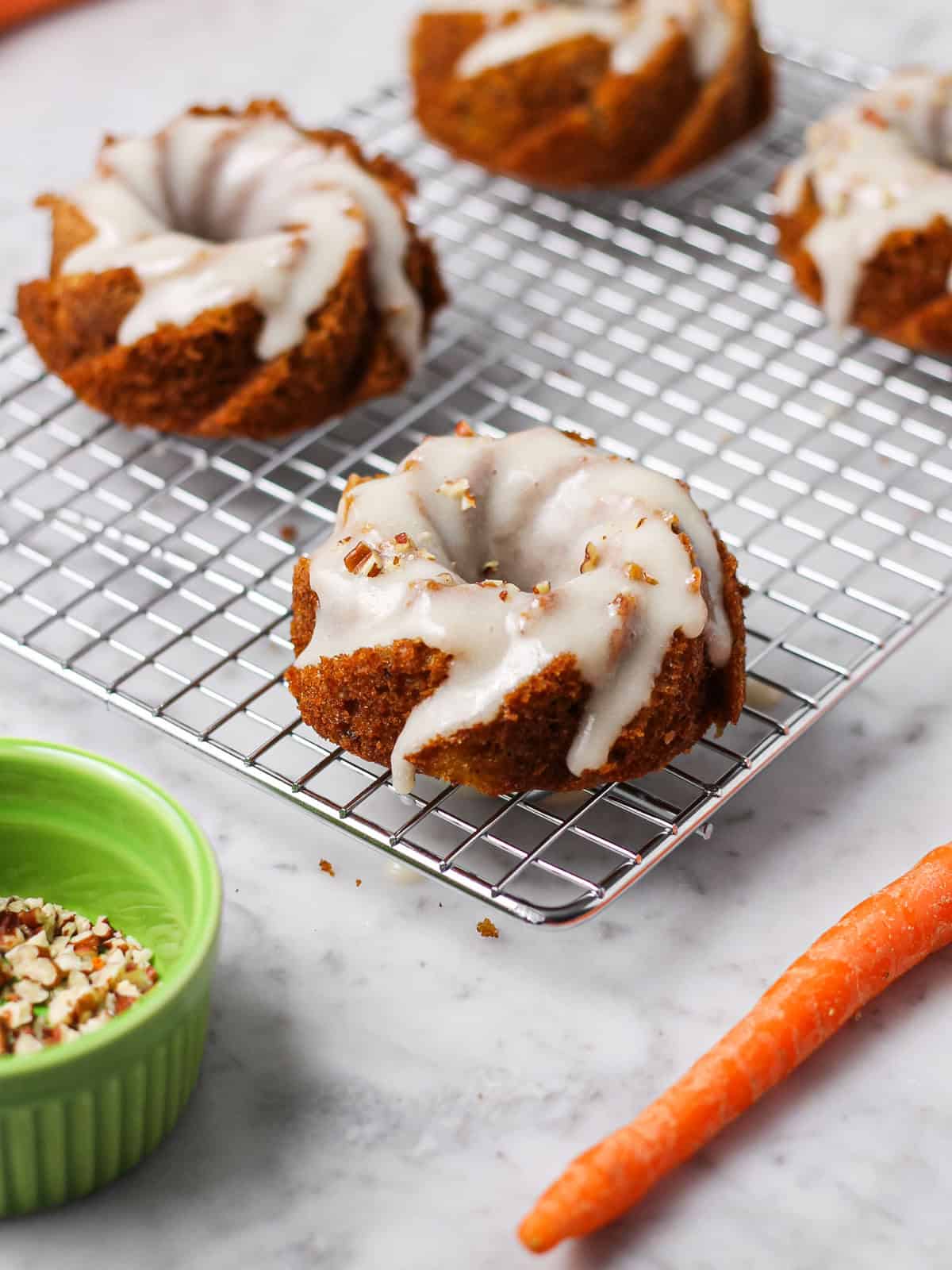 Mini carrot bundt cakes on a cooling rack. Cakes are topped with a white cream cheese glaze.