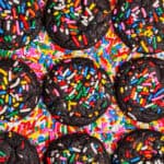 Overhead image of chocolate sprinkle cookies sitting against a background of rainbow sprinkles.