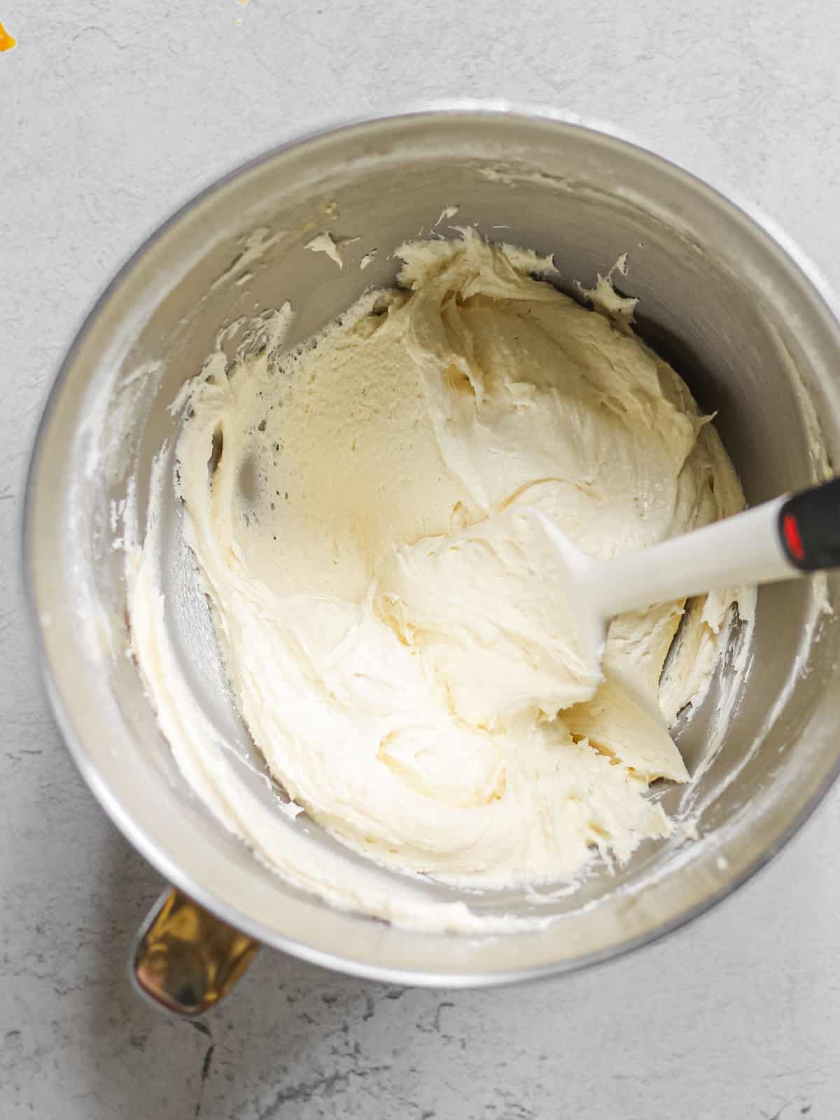 Mixing bowl filled with a smooth, light yellow frosting and a white rubber spatula.