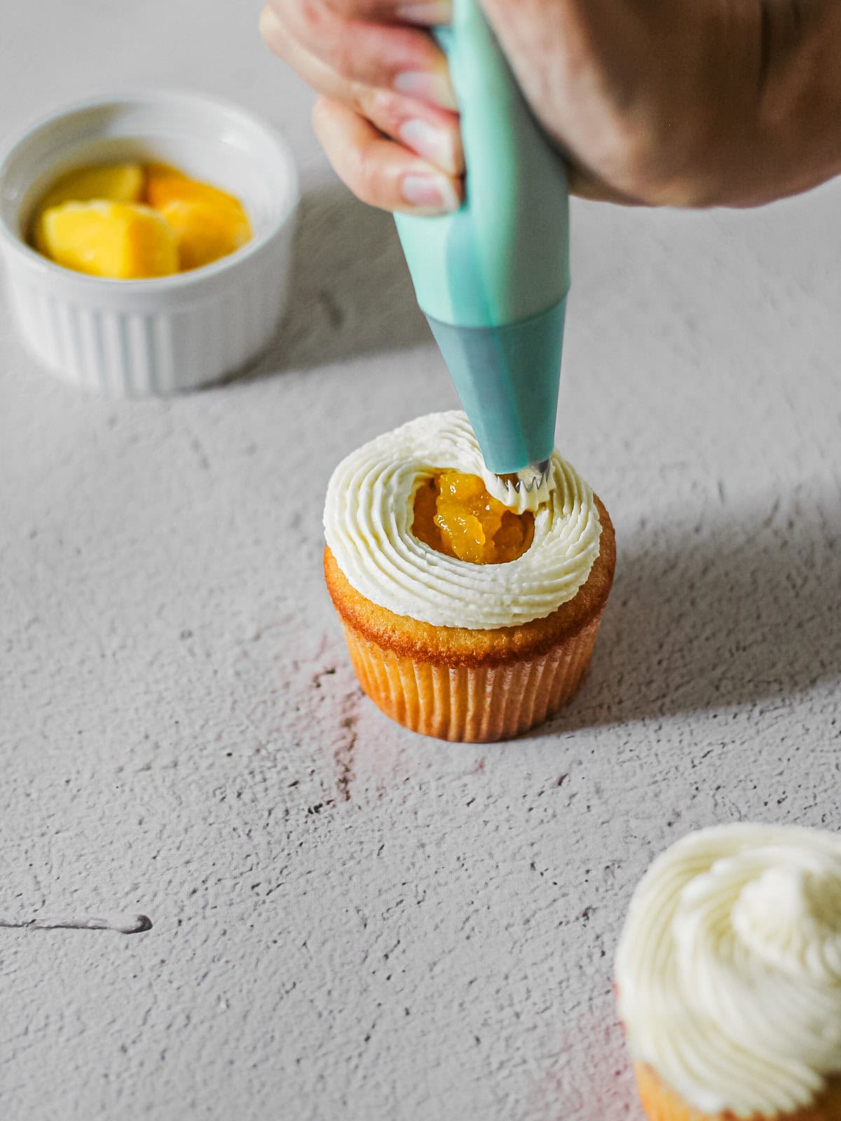 Piping frosting onto cupcakes filled with mango.