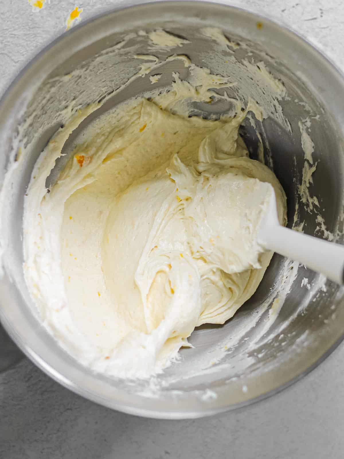 Mixing bowl filled smooth mango buttercream and a white rubber spatula.