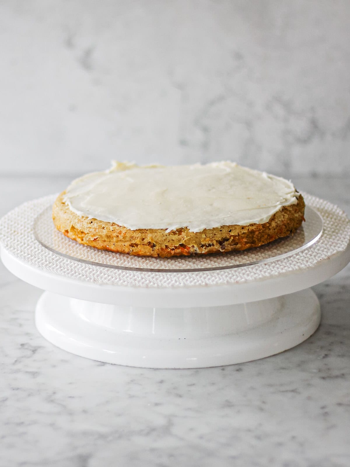 First of three layers of old fashioned carrot cake sitting on a white cake turntable.