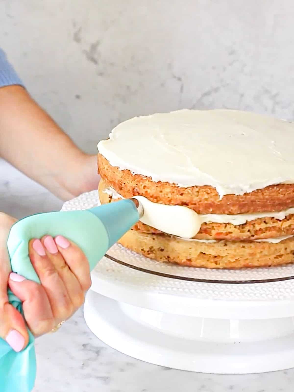 Action shot of frosting the outside of a carrot cake, using cream cheese frosting in a piping bag.