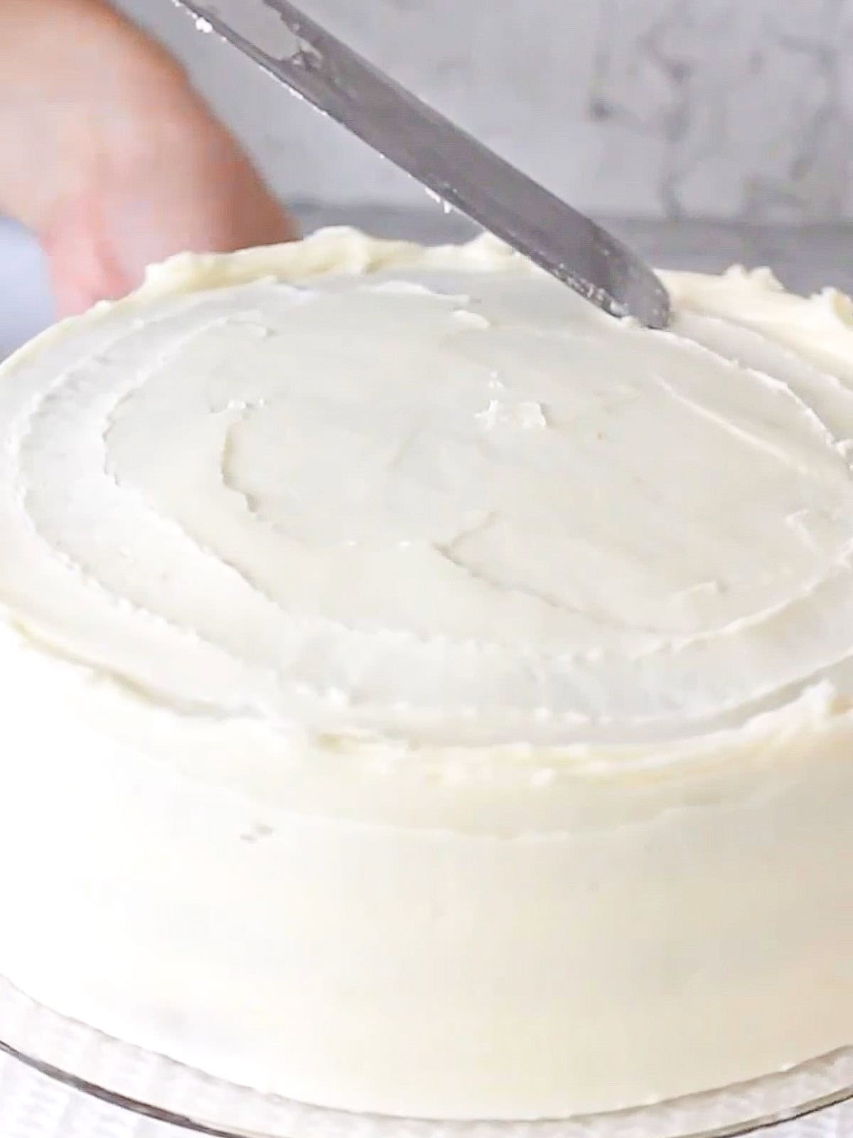 Action shot of decorating the top of a carrot cake with an offset spatula.