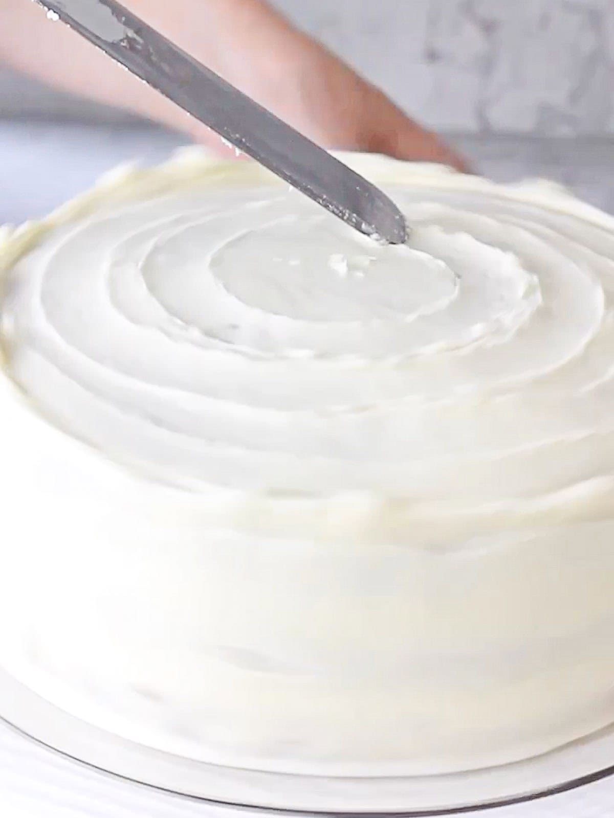 Action shot of decorating the top of a carrot cake with an offset spatula.