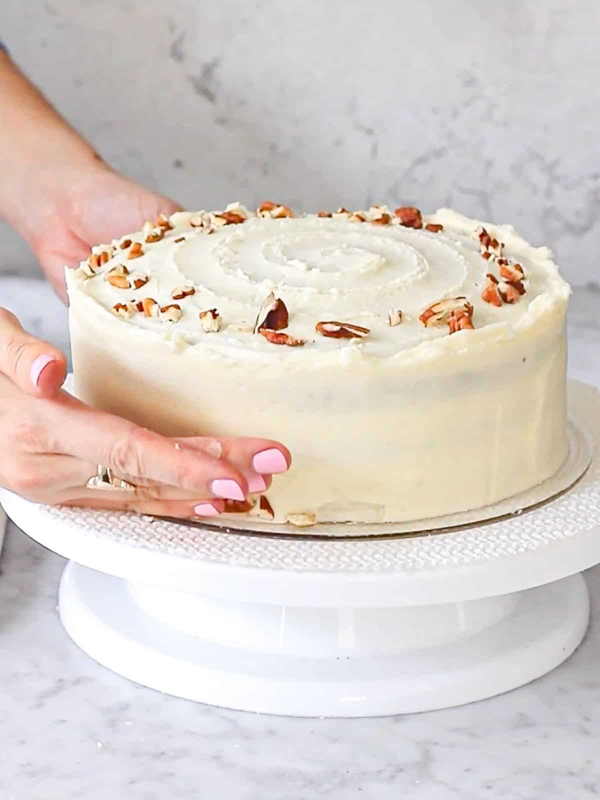 Adding crushed nuts to the base of a frosted carrot cake.