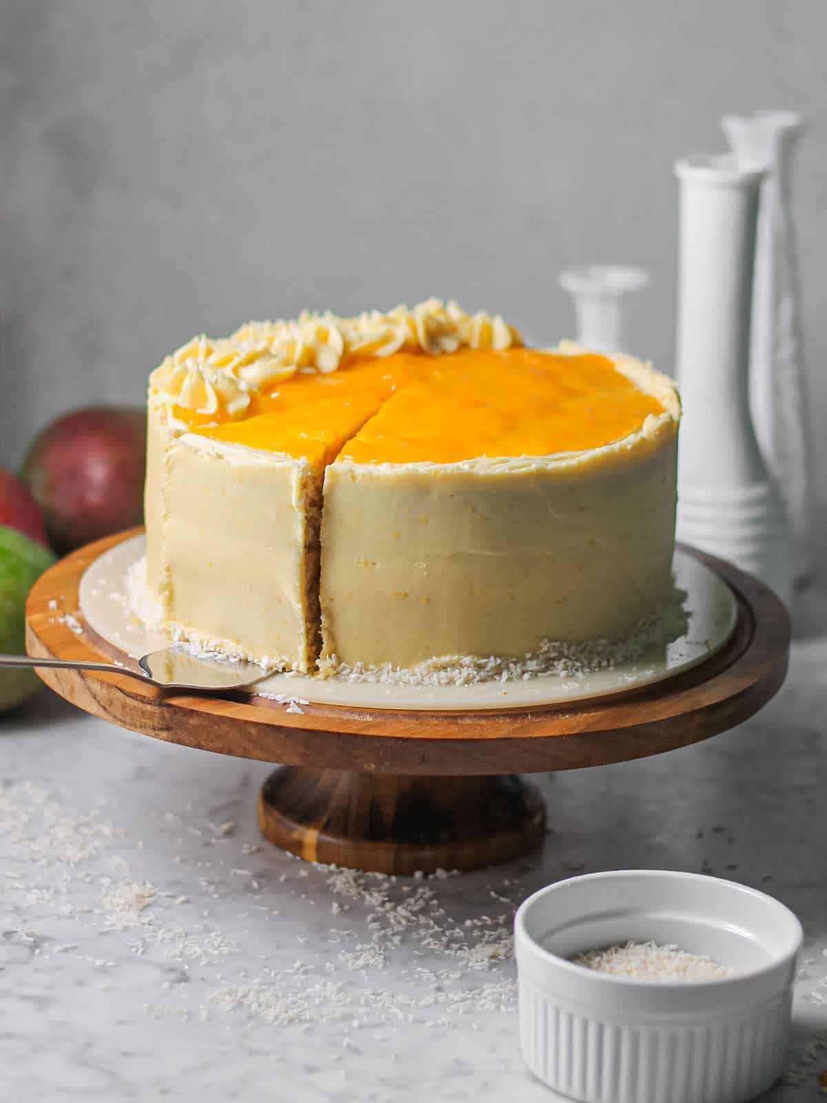 A light yellow mango coconut cake, sitting on a wooden cake stand, with a pie server removing a slice from it.