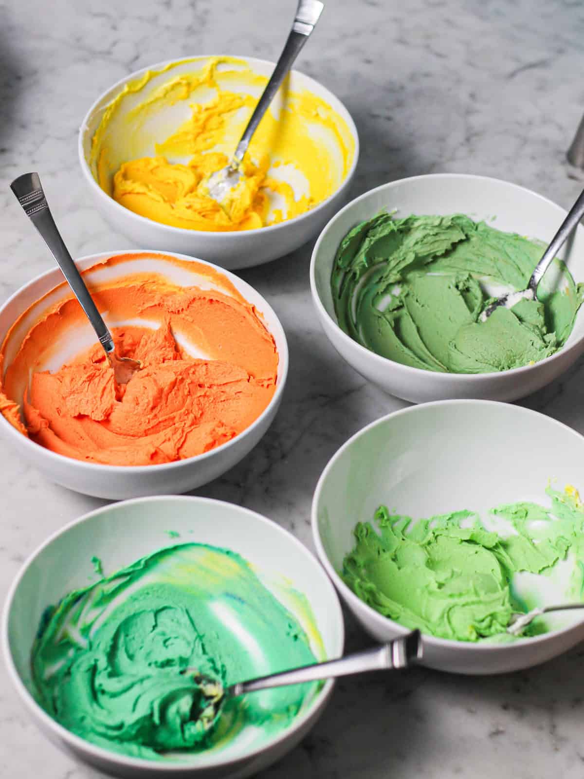 Bowls of colored buttercream for decorating the lemon cake.