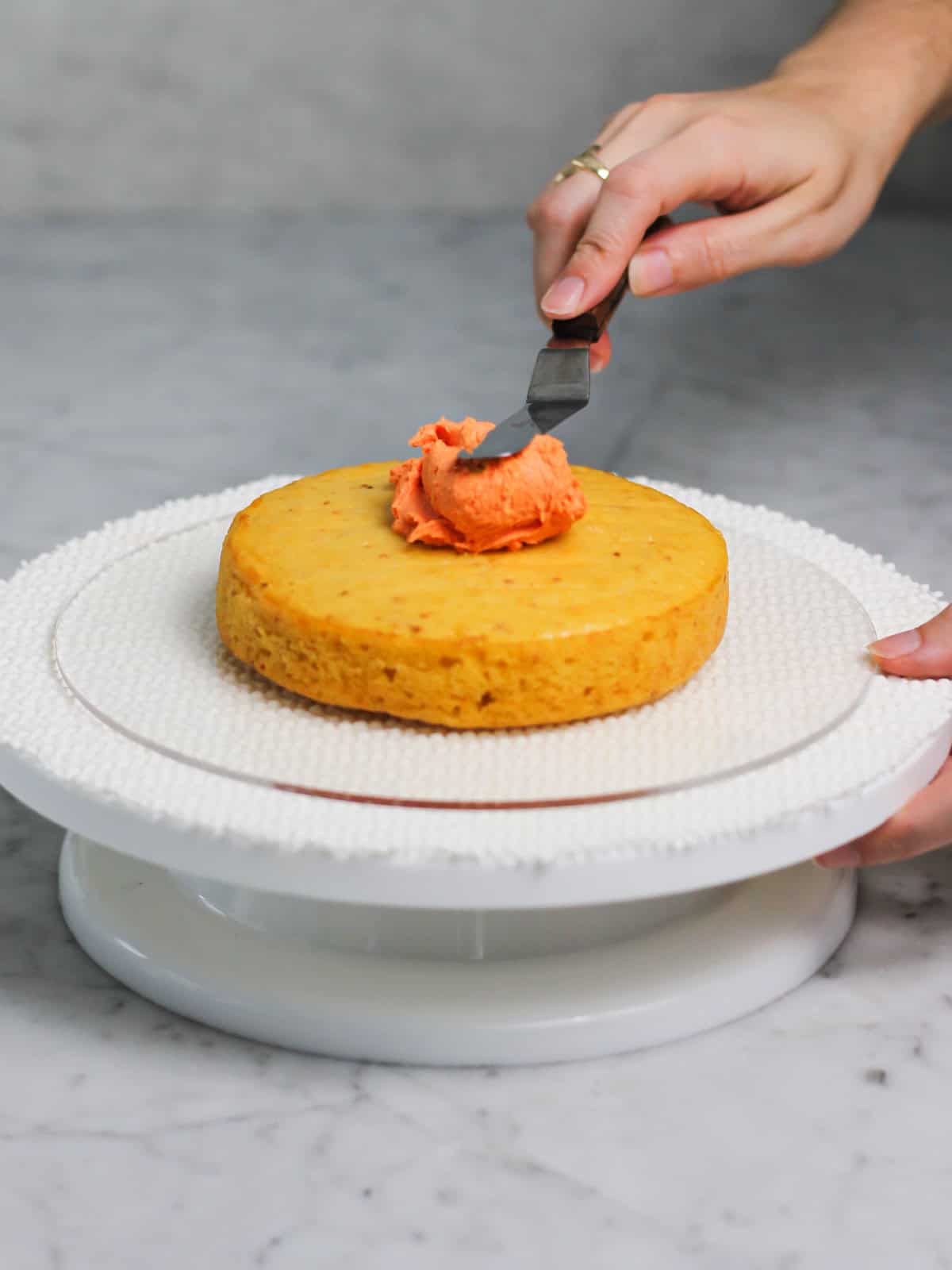 Using an offset spatula to spread orange frosting onto a freshly baked cake.