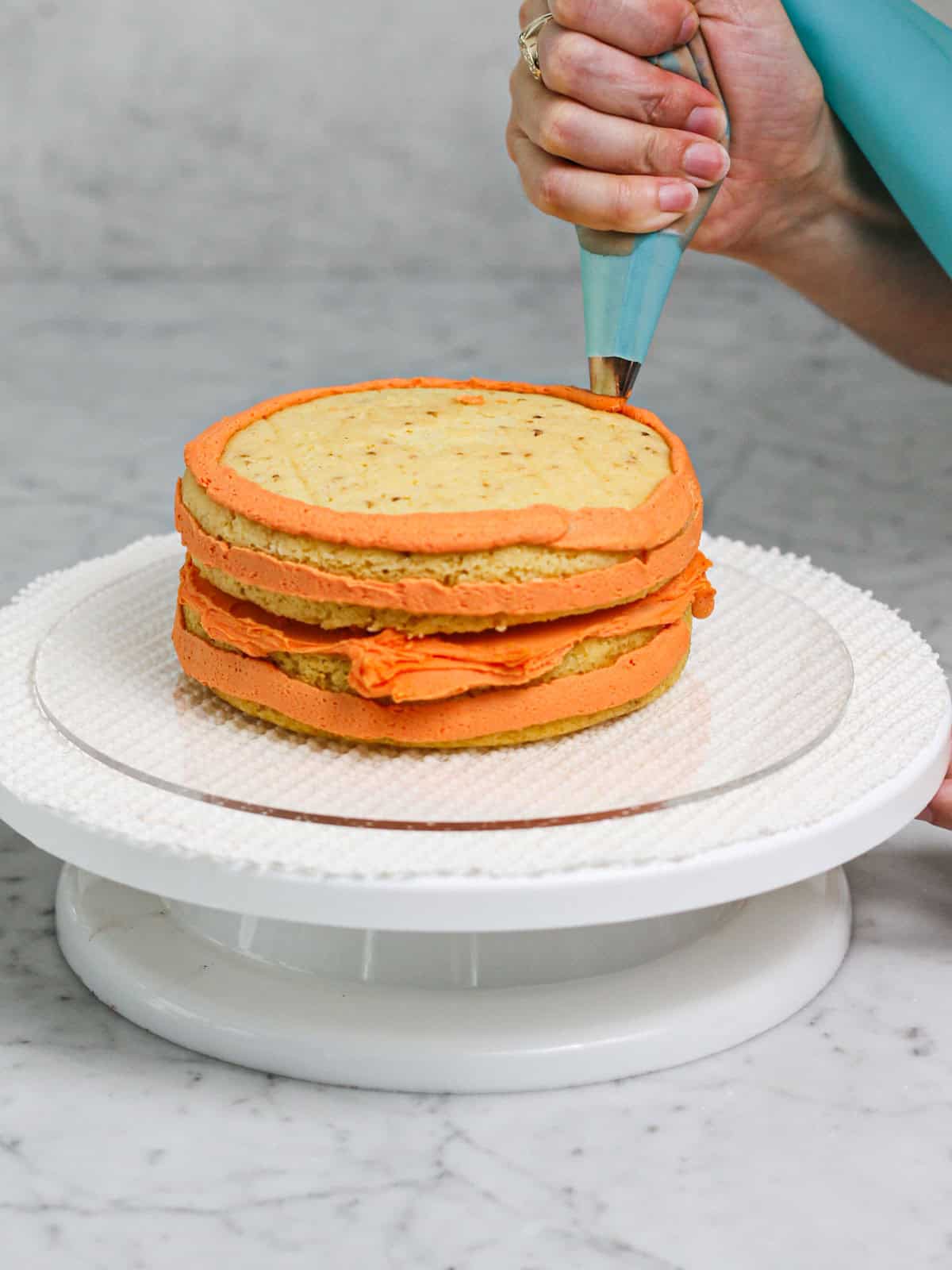 Piping orange frosting onto a freshly baked cake.