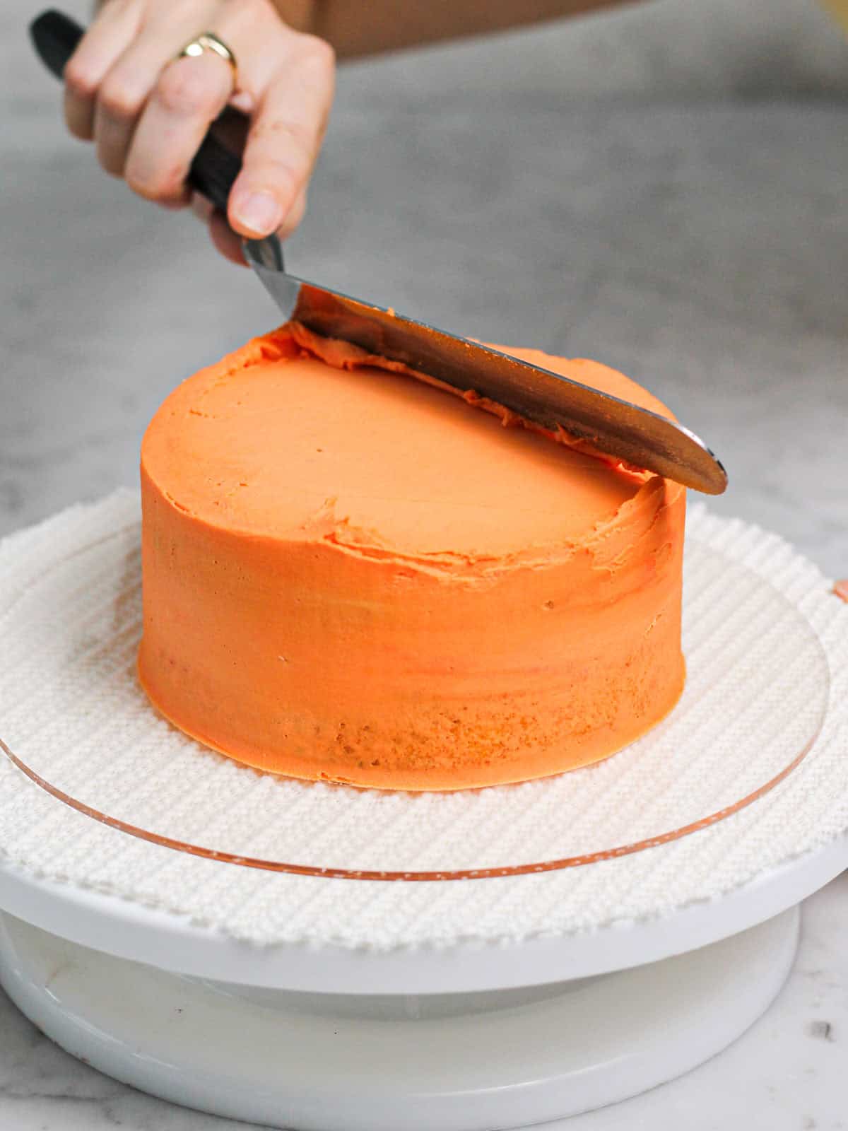 Using an offset spatula to smooth the top of a cake decorated with orange buttercream.