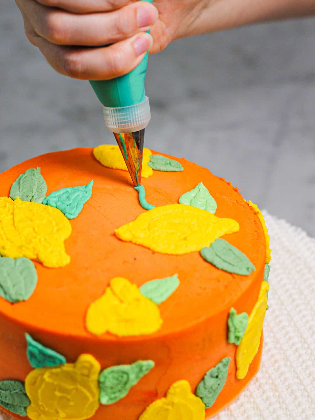 Piping green leaves onto the buttercream lemon cake.