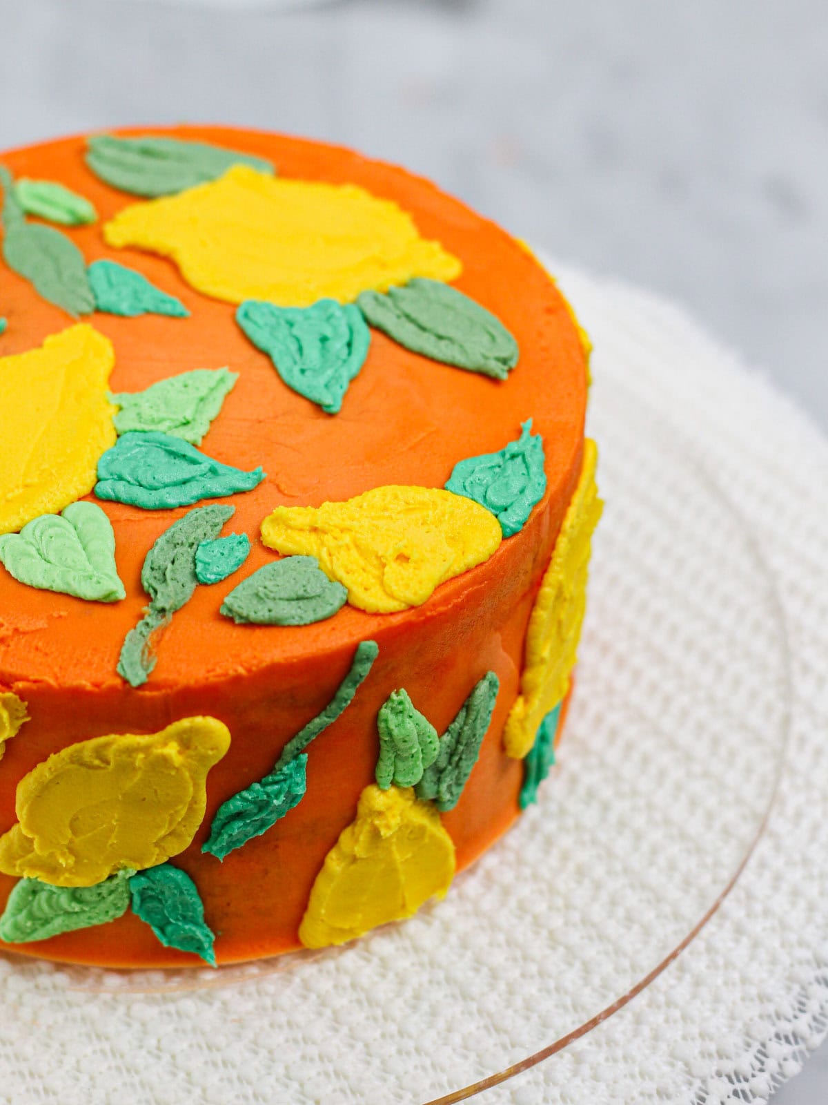 Vibrant orange layered cake decorated with lemons and colorful green leaves for this buttercream lemon cake tutorial.