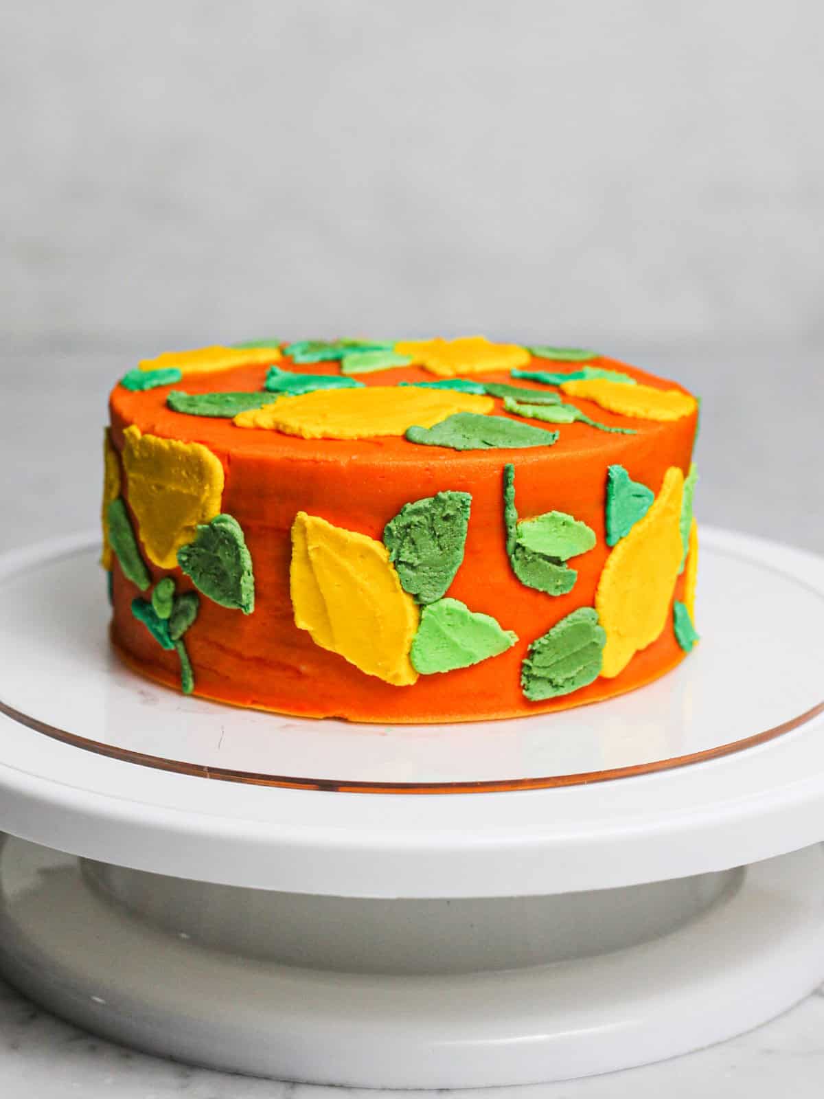 Vibrant orange layered cake decorated with lemons and colorful green leaves for this buttercream lemon cake tutorial.